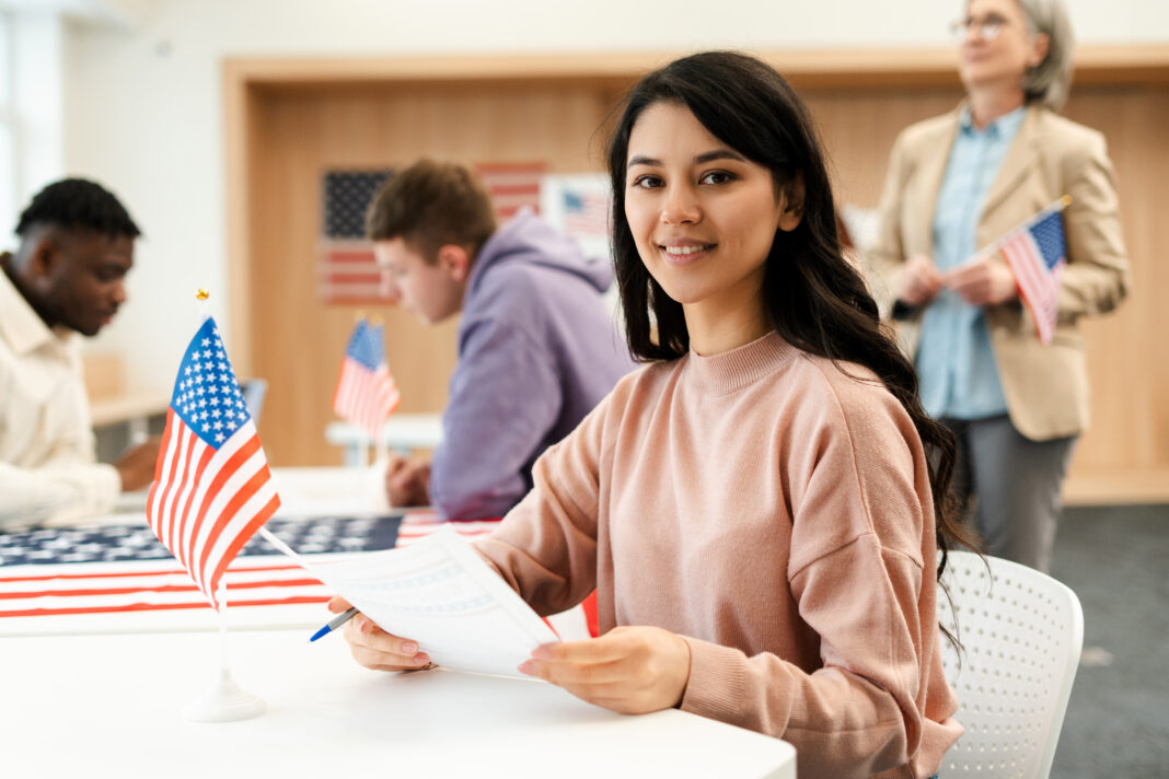 Beautiful, young Asian woman holding ballot sitting at registration table at polling station Student visa